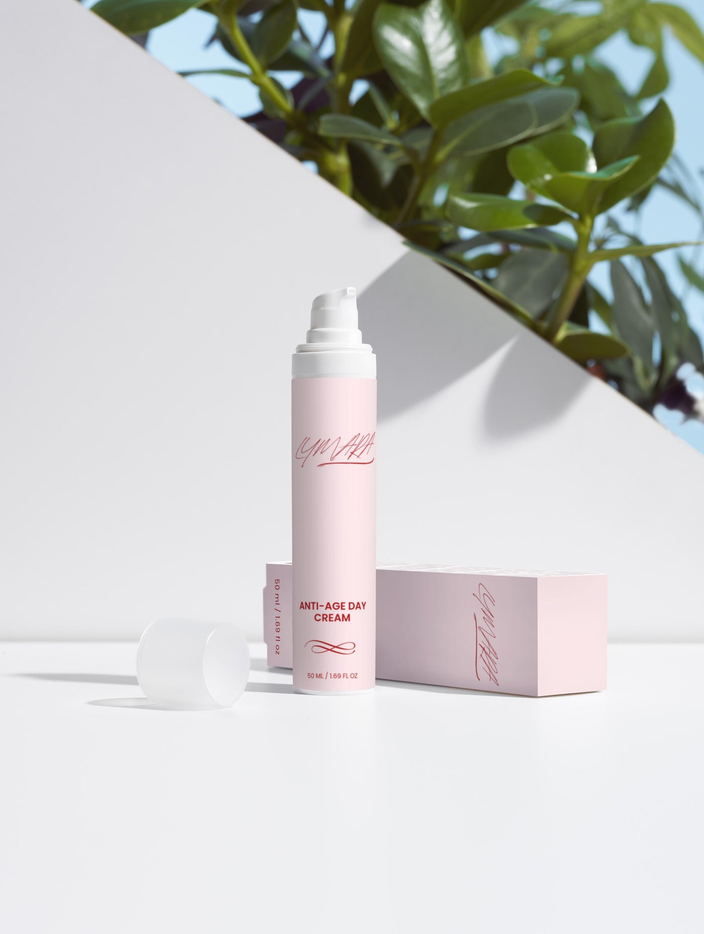 Anti-Age Day Cream in a pink bottle with box on a clean white surface and green foliage in the background.
